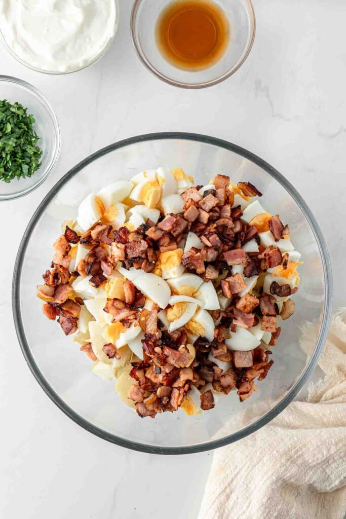 Potato, egg and cooked bacon in a large glass mixing bowl.