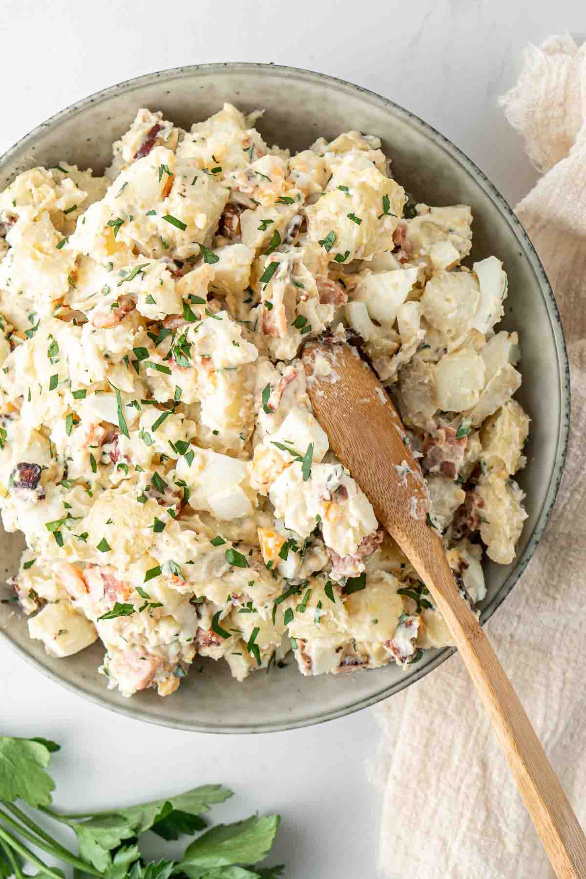 Dairy free potato salad in a serving bowl with a wooden spoon.