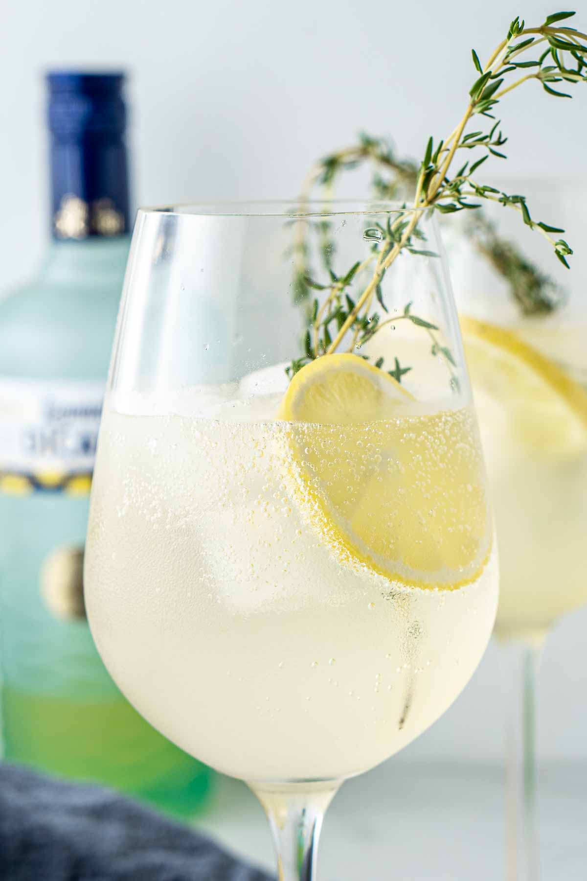 Close up of Limoncello spritz served in a wine glass with lemon and fresh thyme.