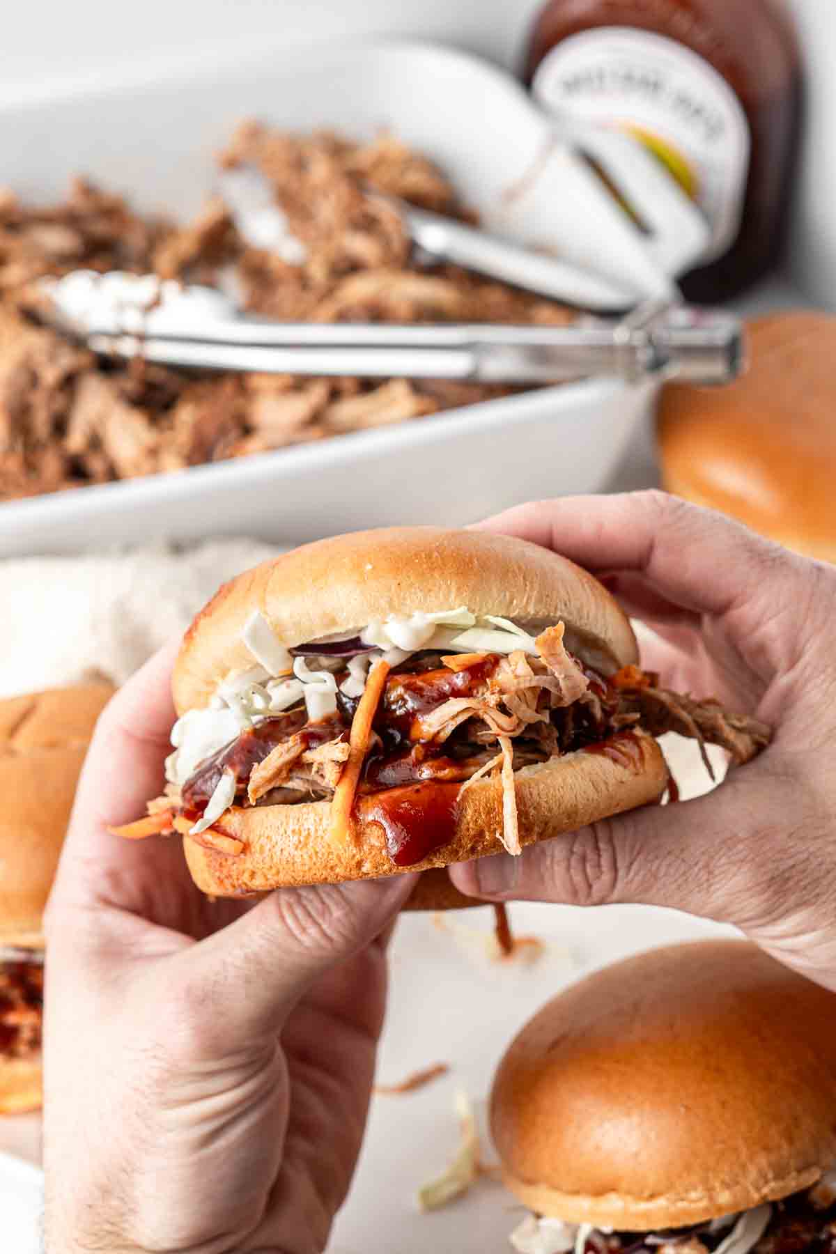Hands holding a pulled pork burger with BBQ sauce. 