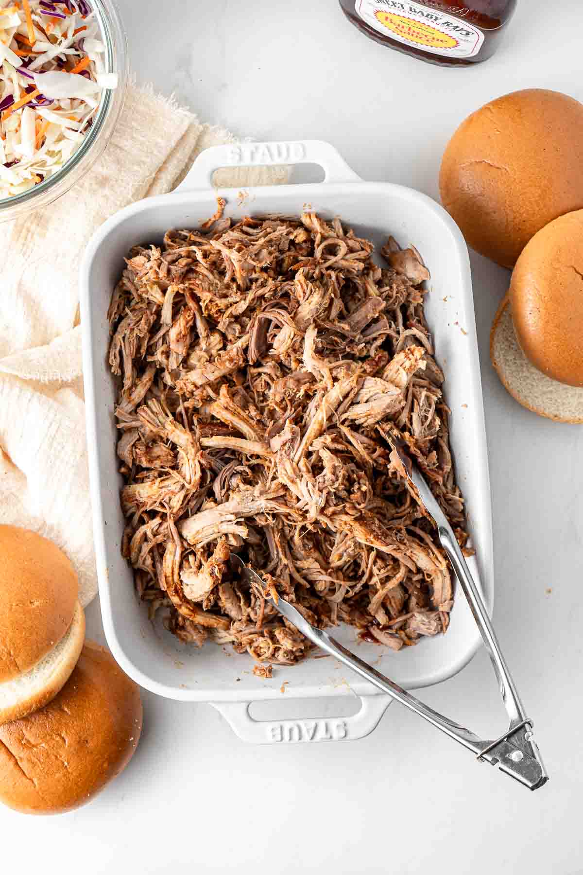 BBQ pulled pork in a casserole dish with tongs for serving. 