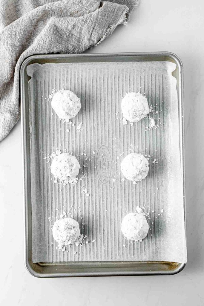 Chocolate cookie dough balls coated in powdered sugar on a baking tray.