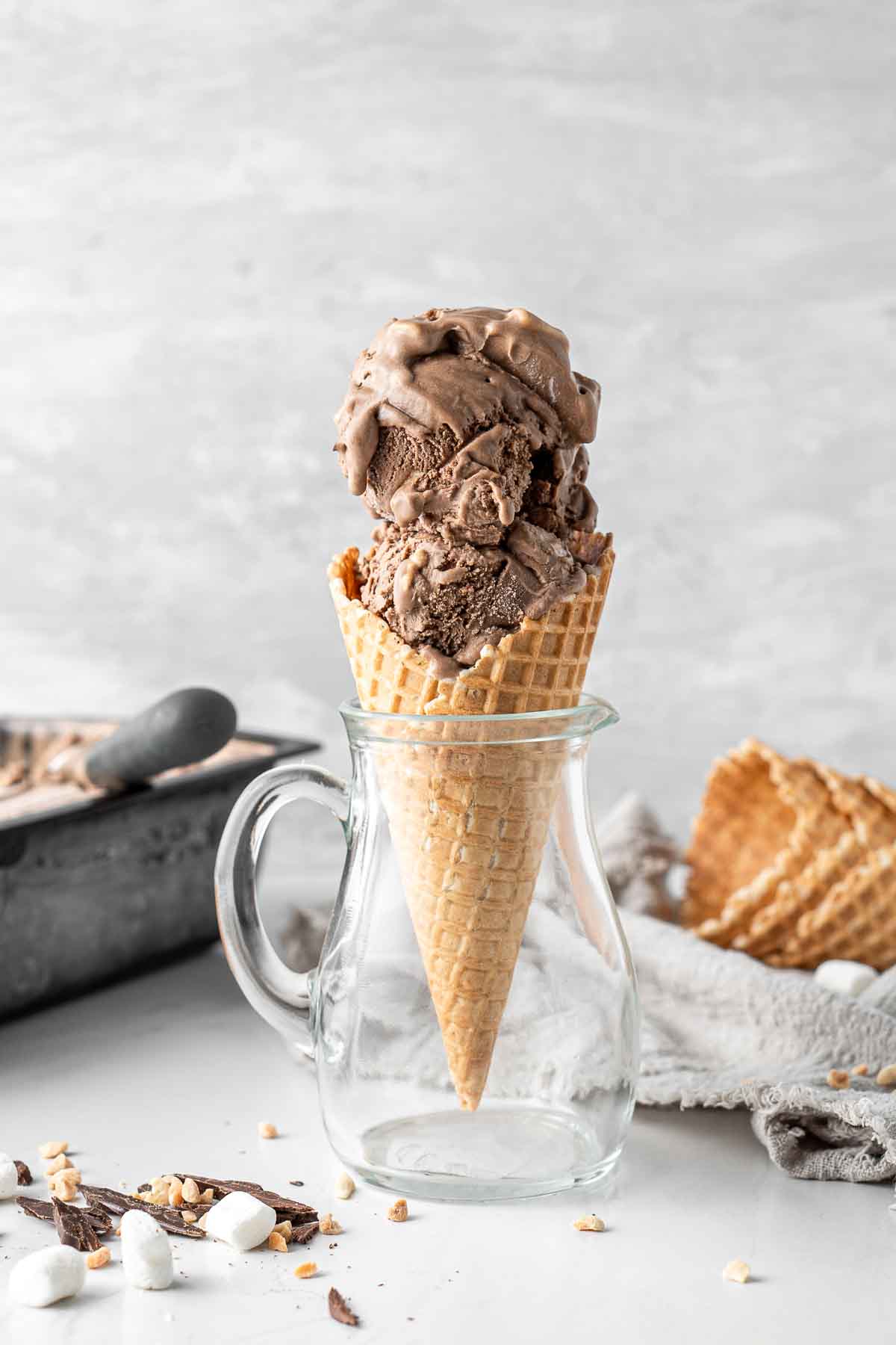 Dairy free chocolate ice cream in a waffle cone standing upright in a glass jug.