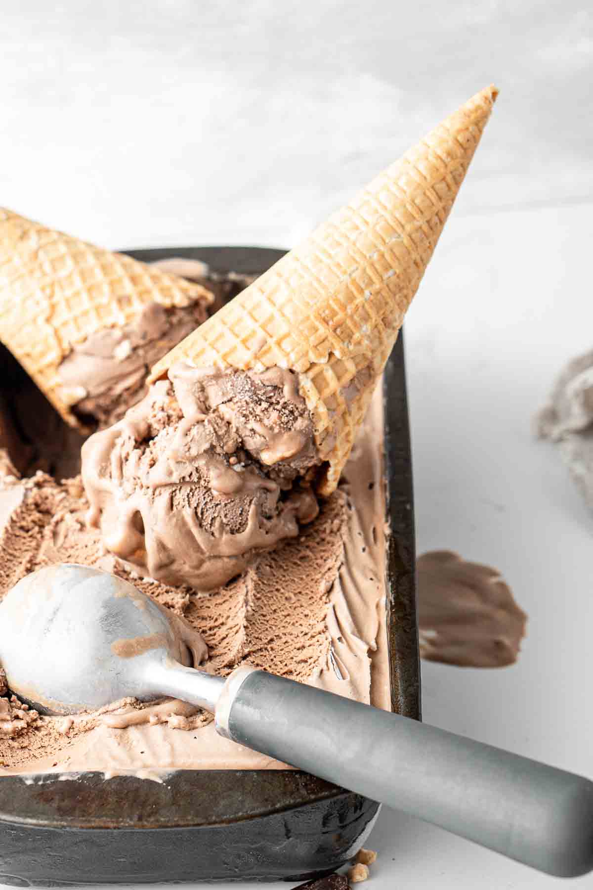 Vegan rocky road ice cream in a waffle cone upside down in the ice cream container. 