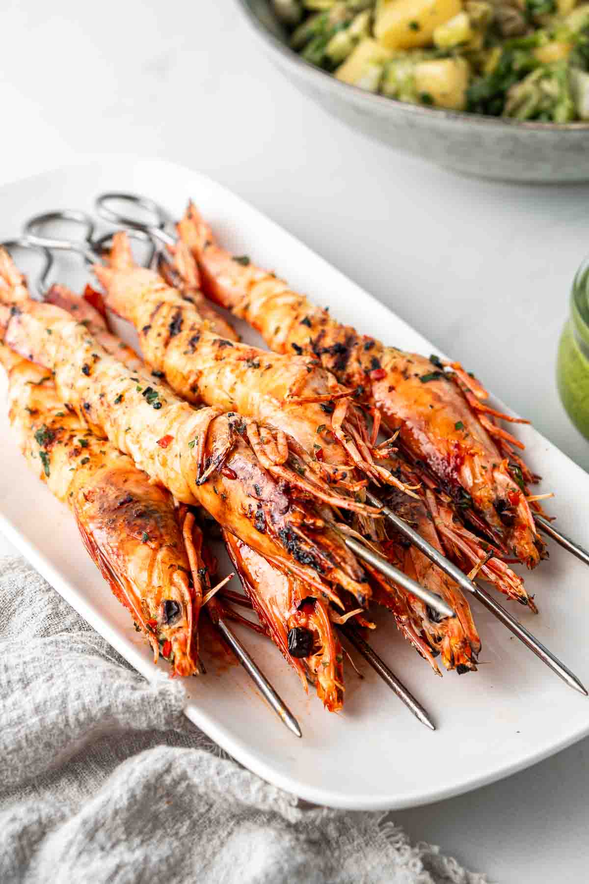 Grilled prawns on metal skewers on a white serving plate.