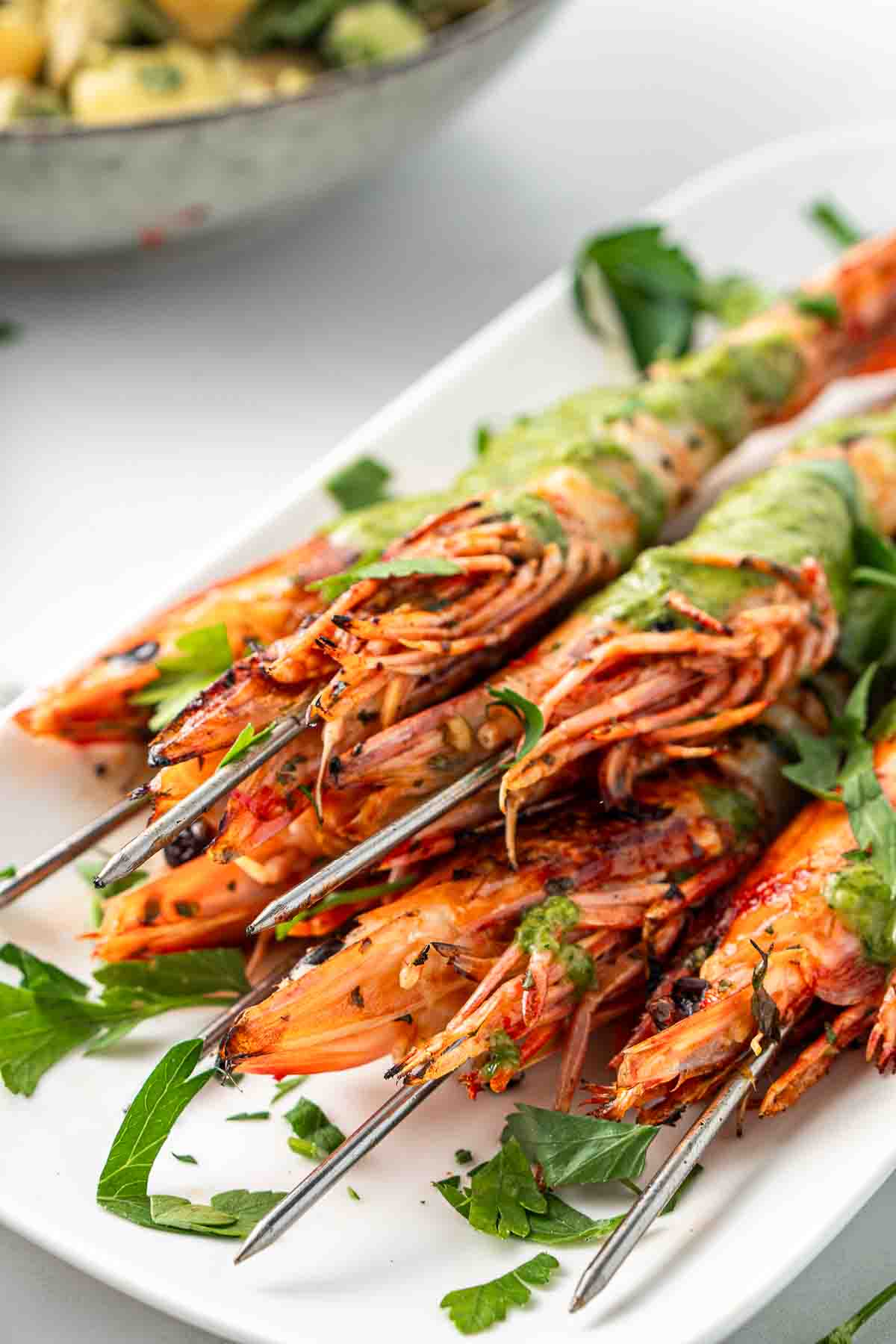 Close up of grilled prawns on skewers on a white serving plate.