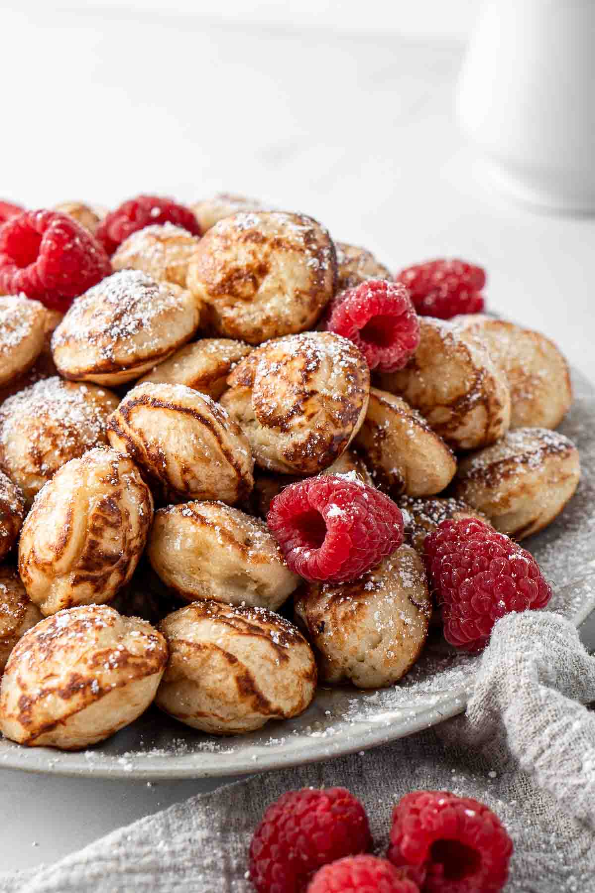 Close up of a plate of poffertjes and raspberries with a dusting of icing sugar.