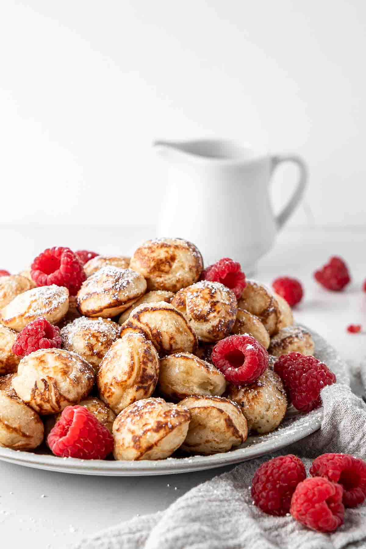 Pile of poffertjes with raspberries and icing sugar on a plate.