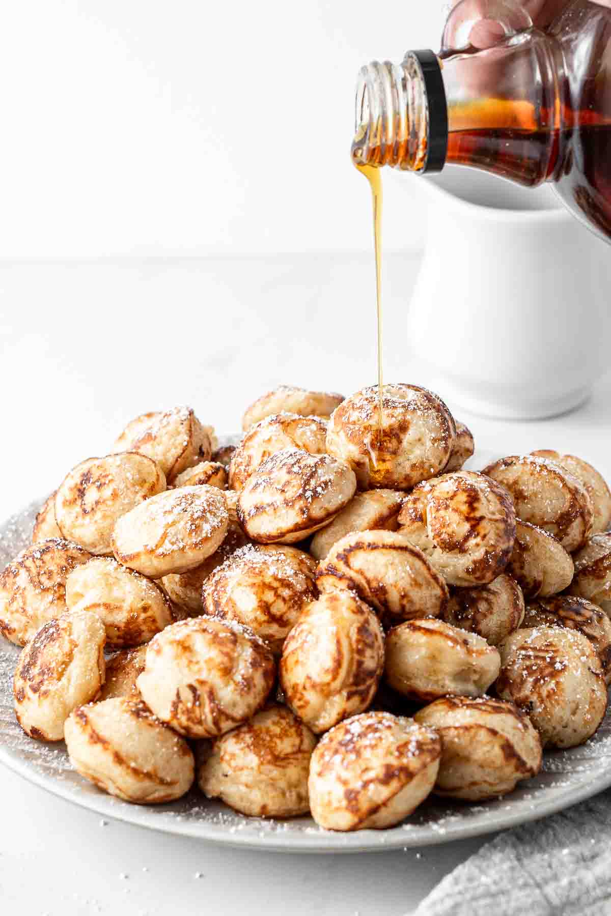 Plate of poffertjes with maple syrup being drizzled over the top. 