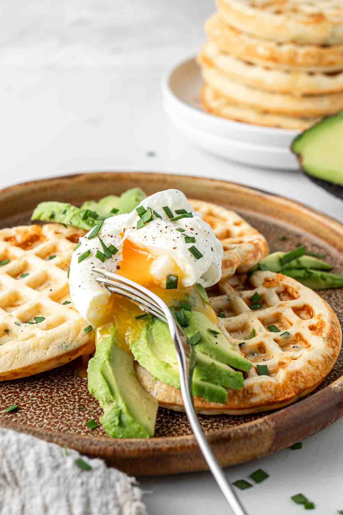 Close up of poached egg and avocado on savoury waffles with fresh chives.