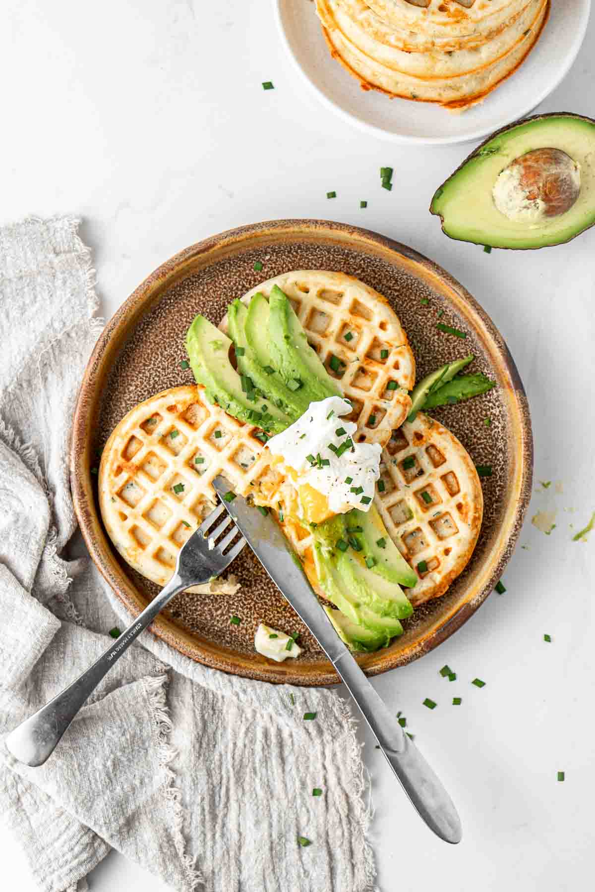 Poached egg and avocado on savoury cheese and chive waffles with fresh chives.