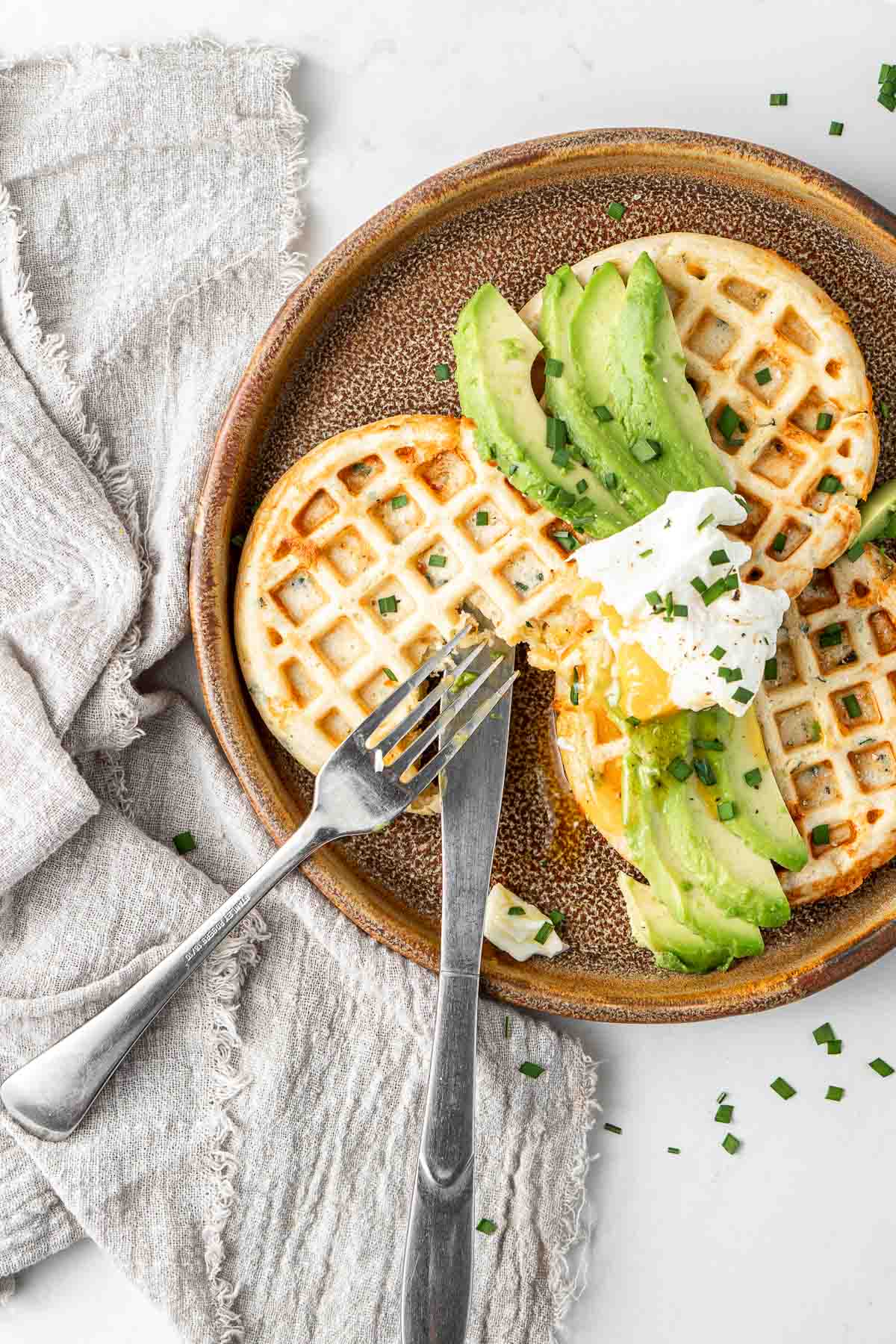 Close up of savoury waffles with avocado and eggs with a knife and fork. 