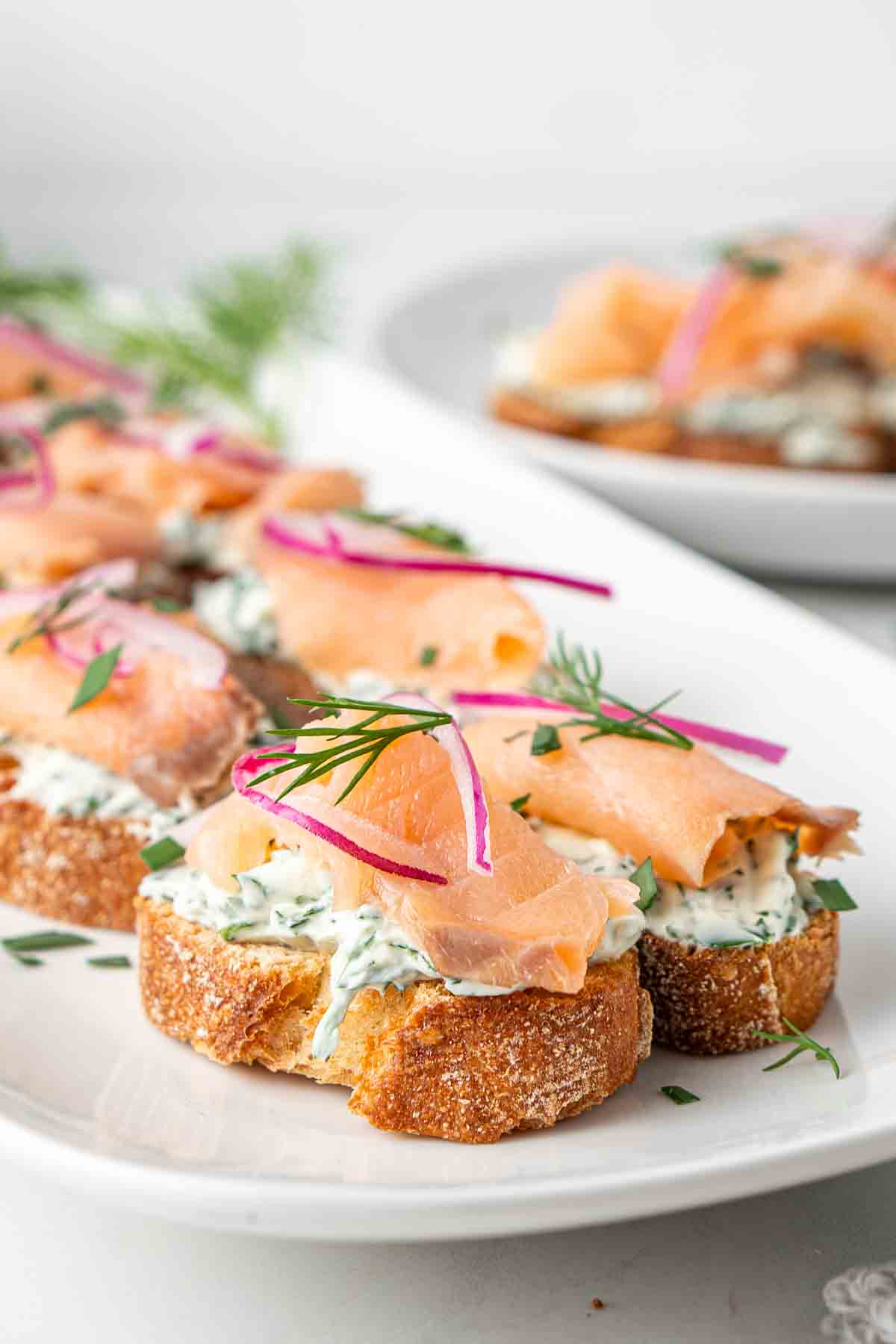 Close up of smoked salmon crostini on a white serving platter with pickled onion and chives.