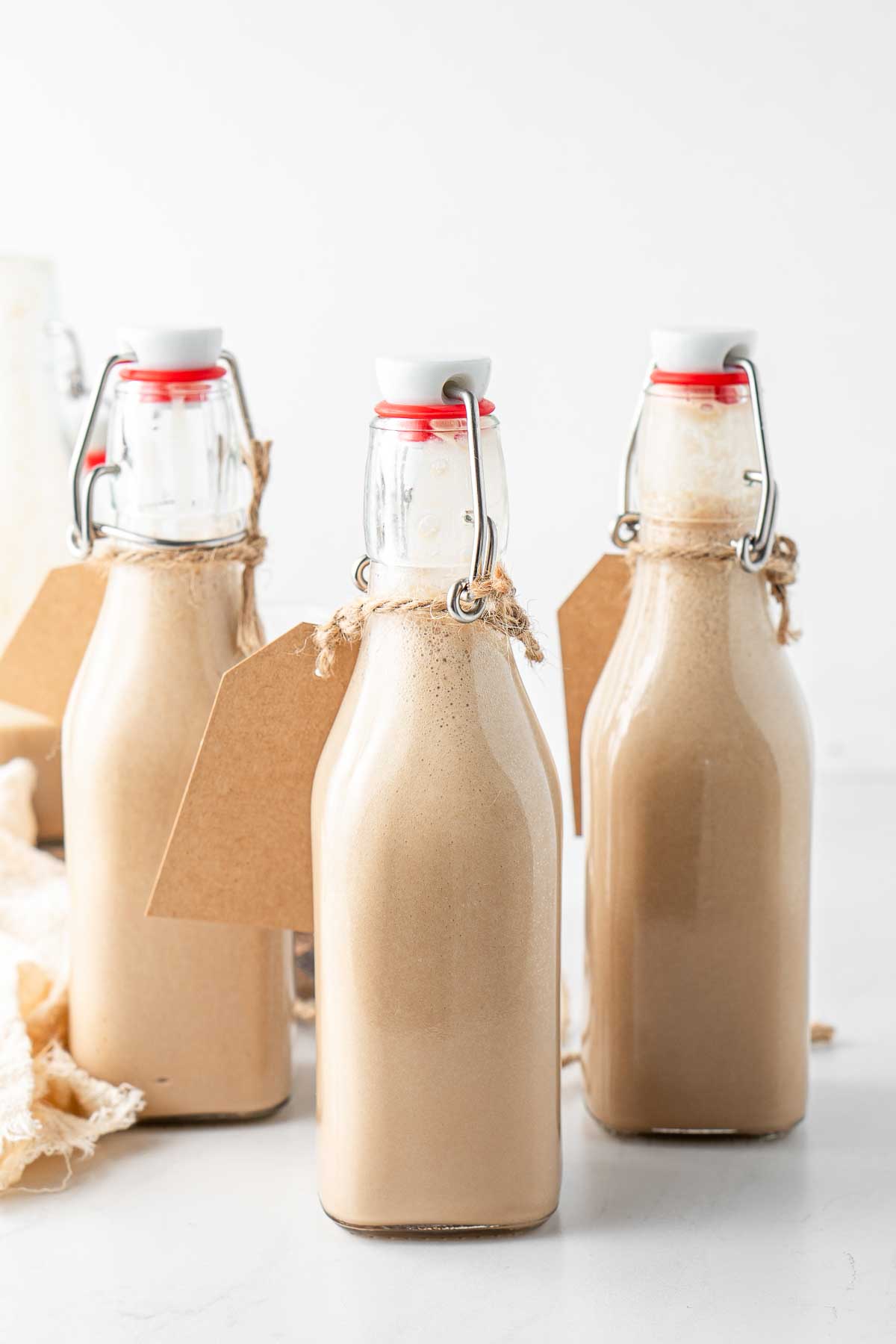 Three bottles of homemade baileys with gift tags.