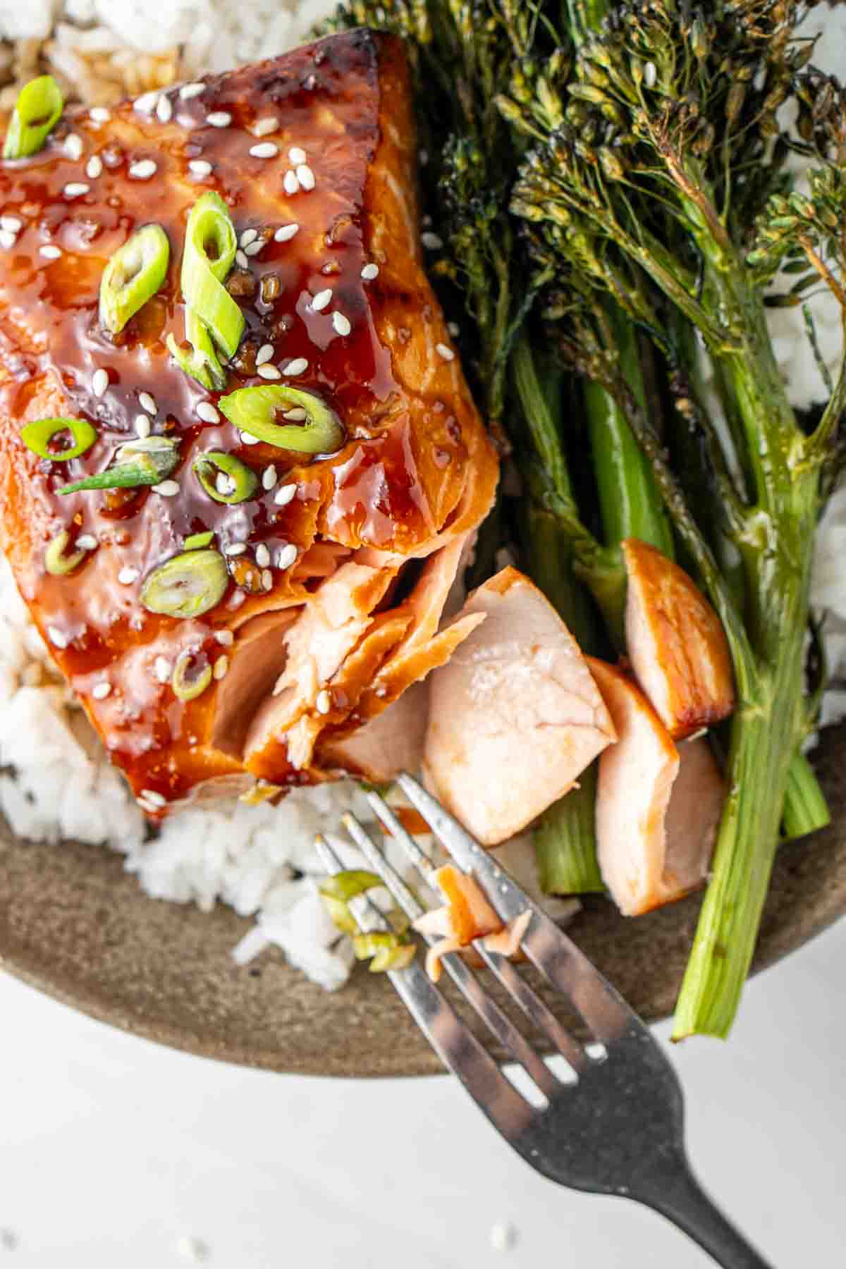 Close up of air fryer teriyaki salmon being flaked with a fork in a bowl with rice and broccolini. 