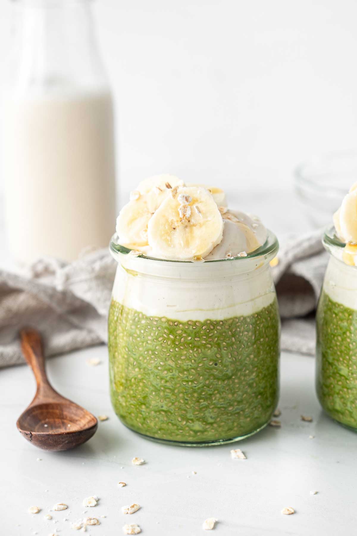 Matcha chia pudding in a glass jar with yoghurt and banana slices with a wooden spoon. 