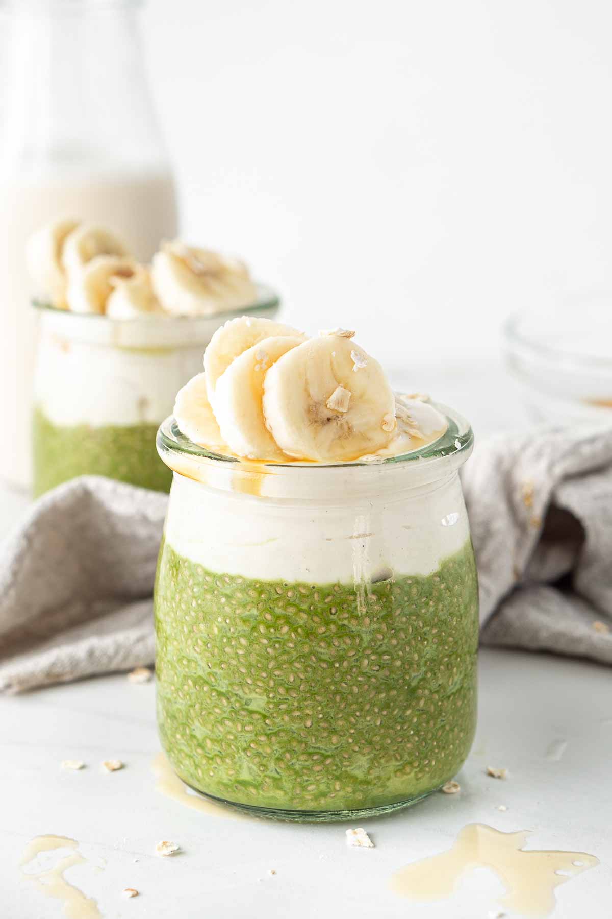 Close up of a matcha chia pudding in a glass jar with yoghurt and banana slices.