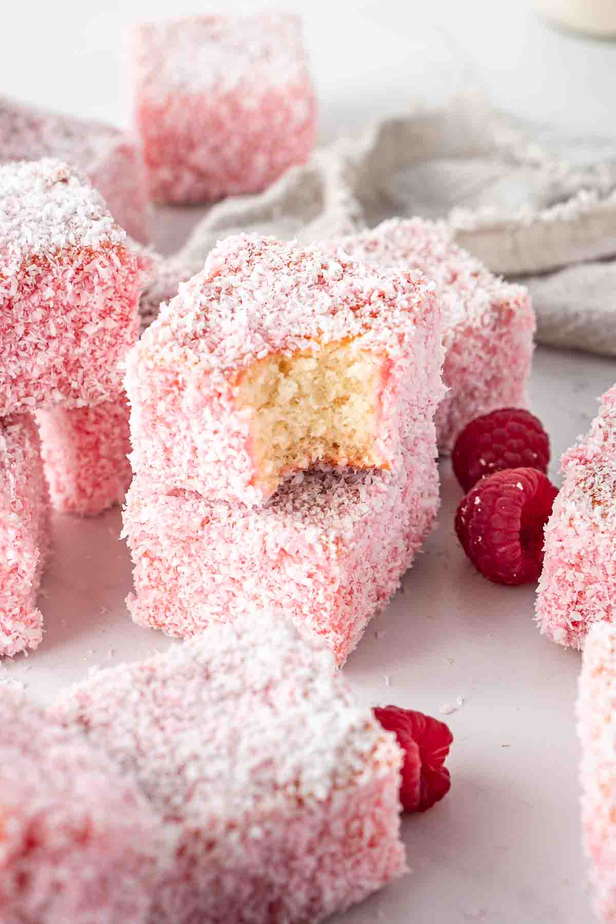 Plain raspberry lamingtons with fresh raspberries and one with a bite taken.