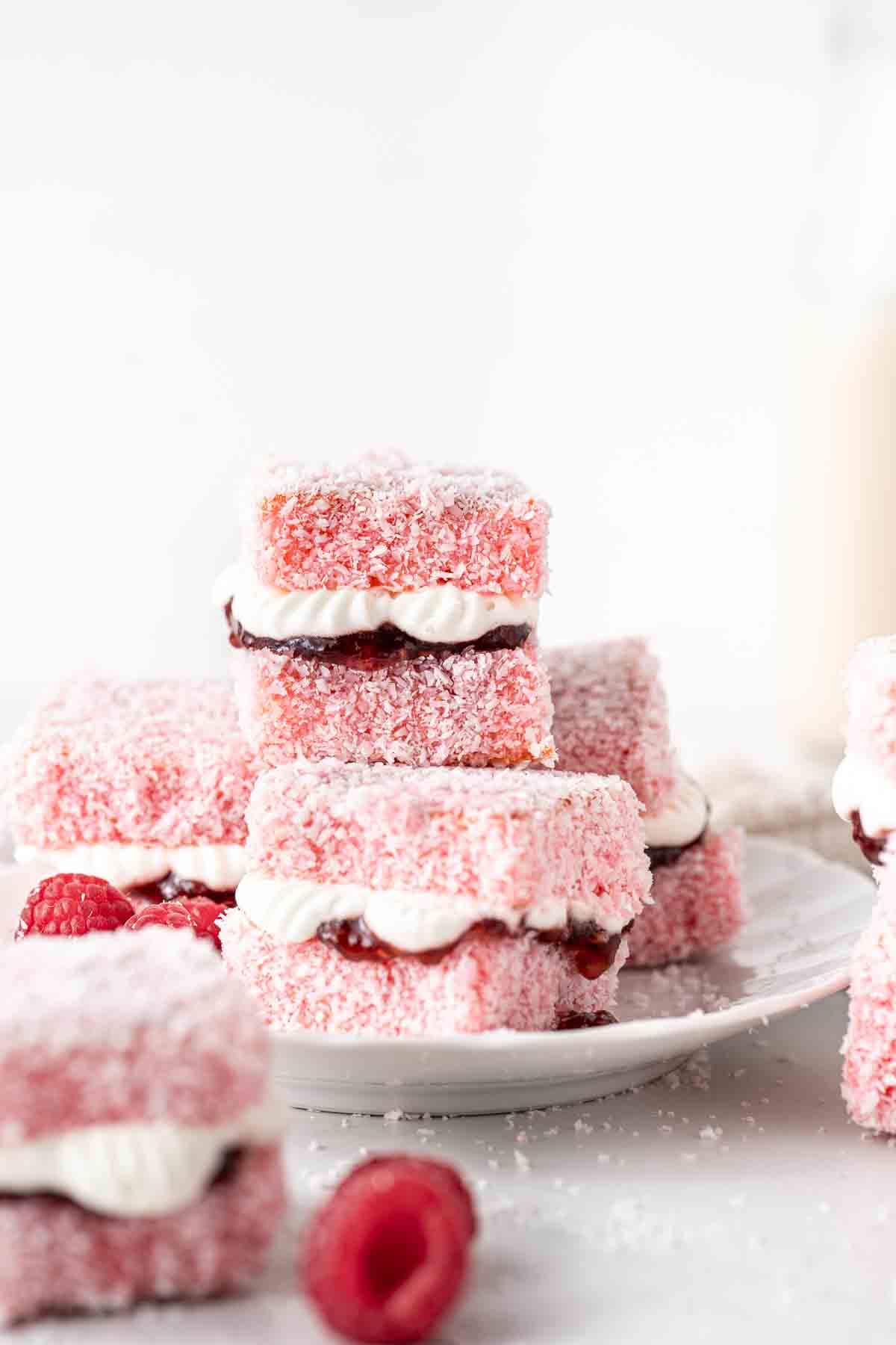 Raspberry lamingtons sandwiched with jam and cream on a white plate.