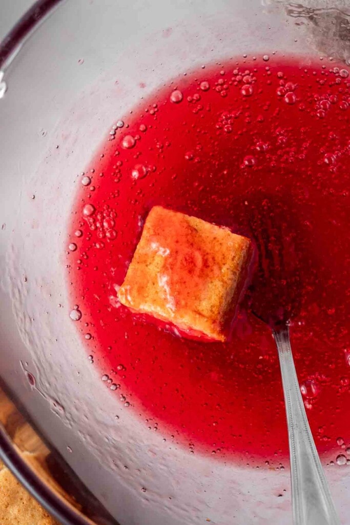 Cake square being dunked into raspberry jelly.