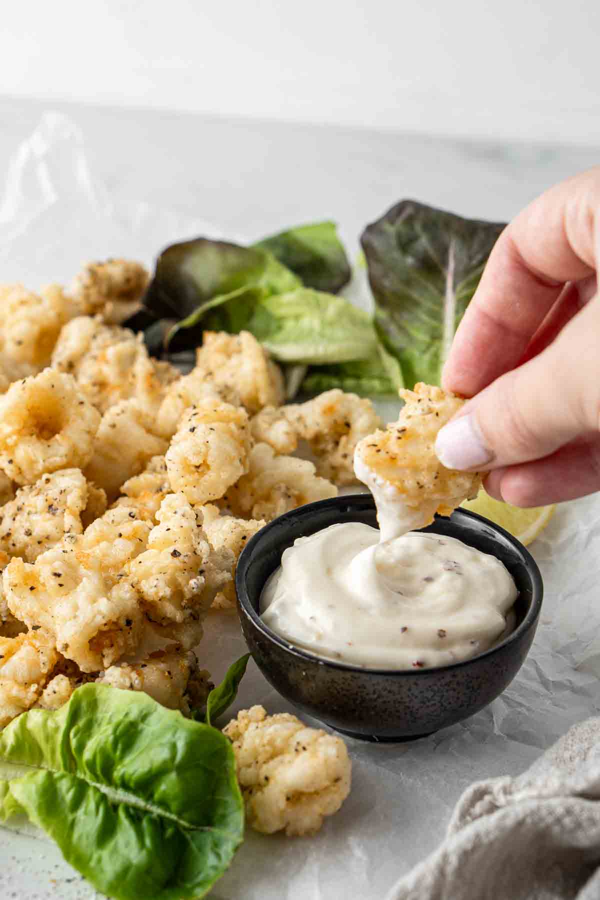 Piece of salt and pepper squid being dipped into garlic aioli. 