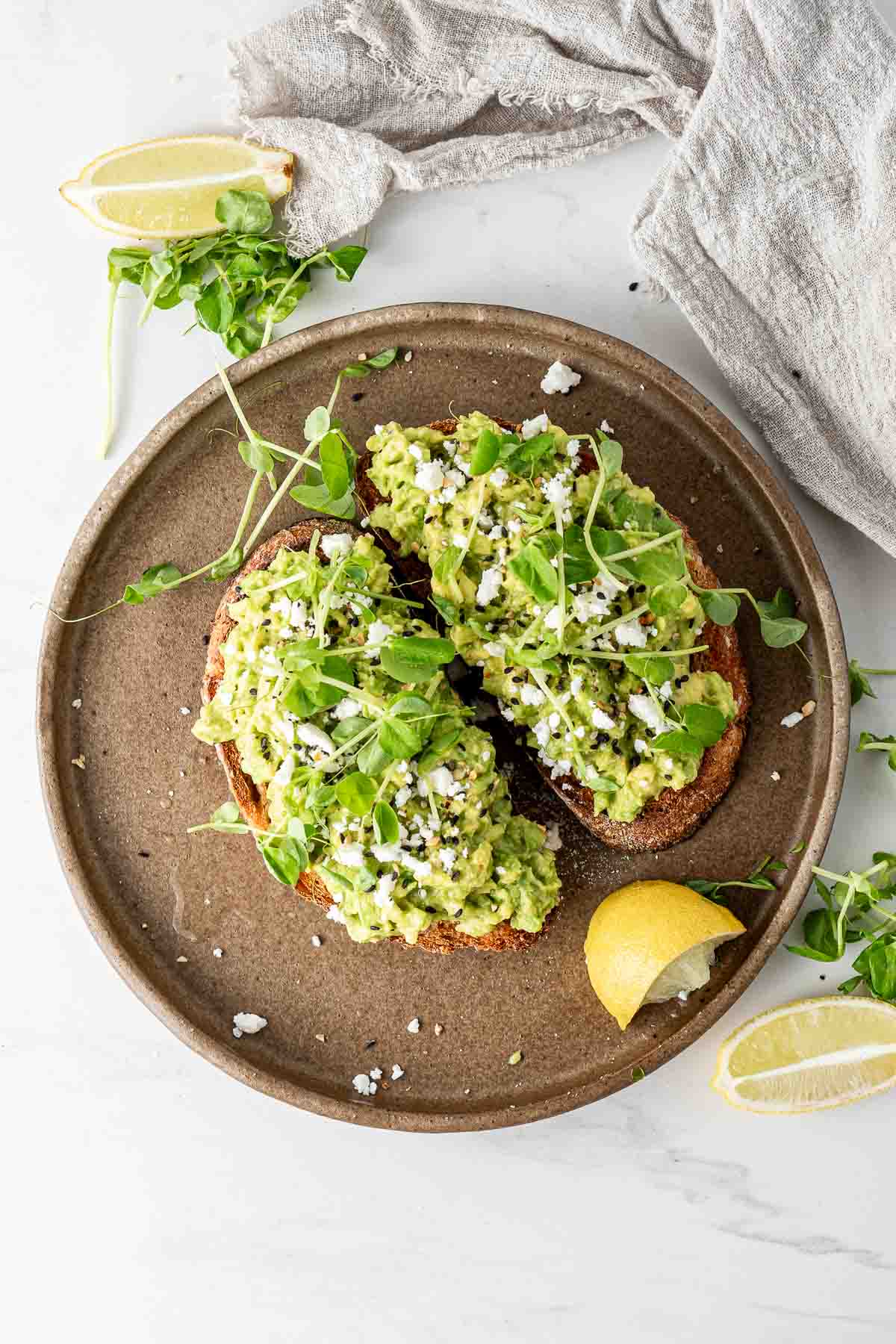 A plate of avocado toast with lemon and sprouts.