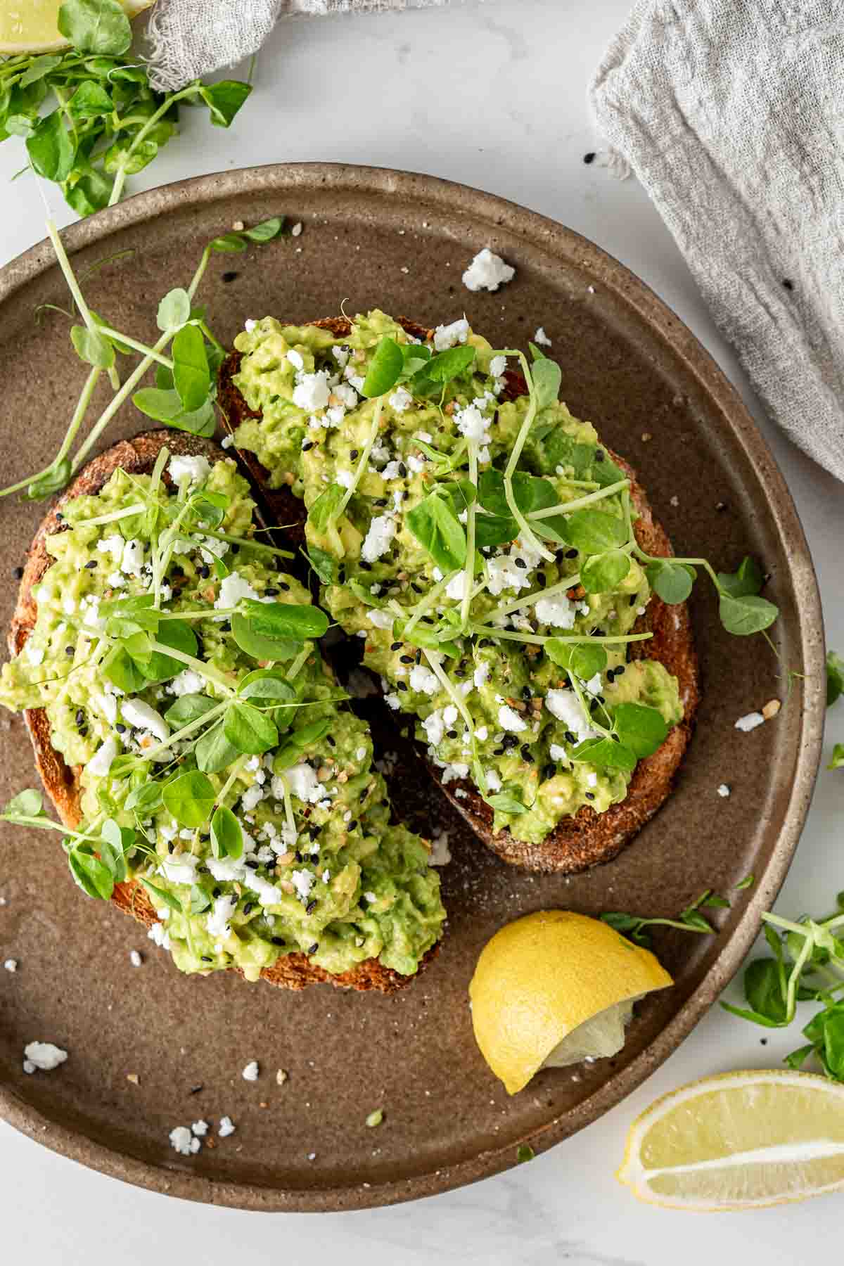Avocado on toast on a brown plate with sprouts and everything bagel seasoning.