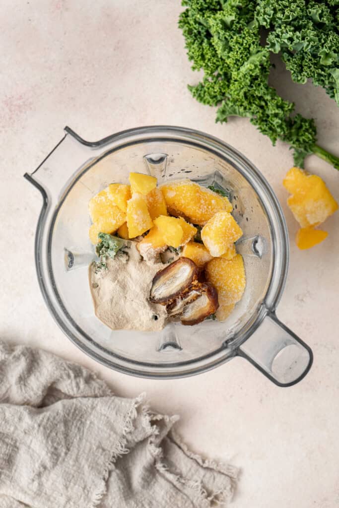 All ingredients for the mango kale smoothie in the jug of a blender.