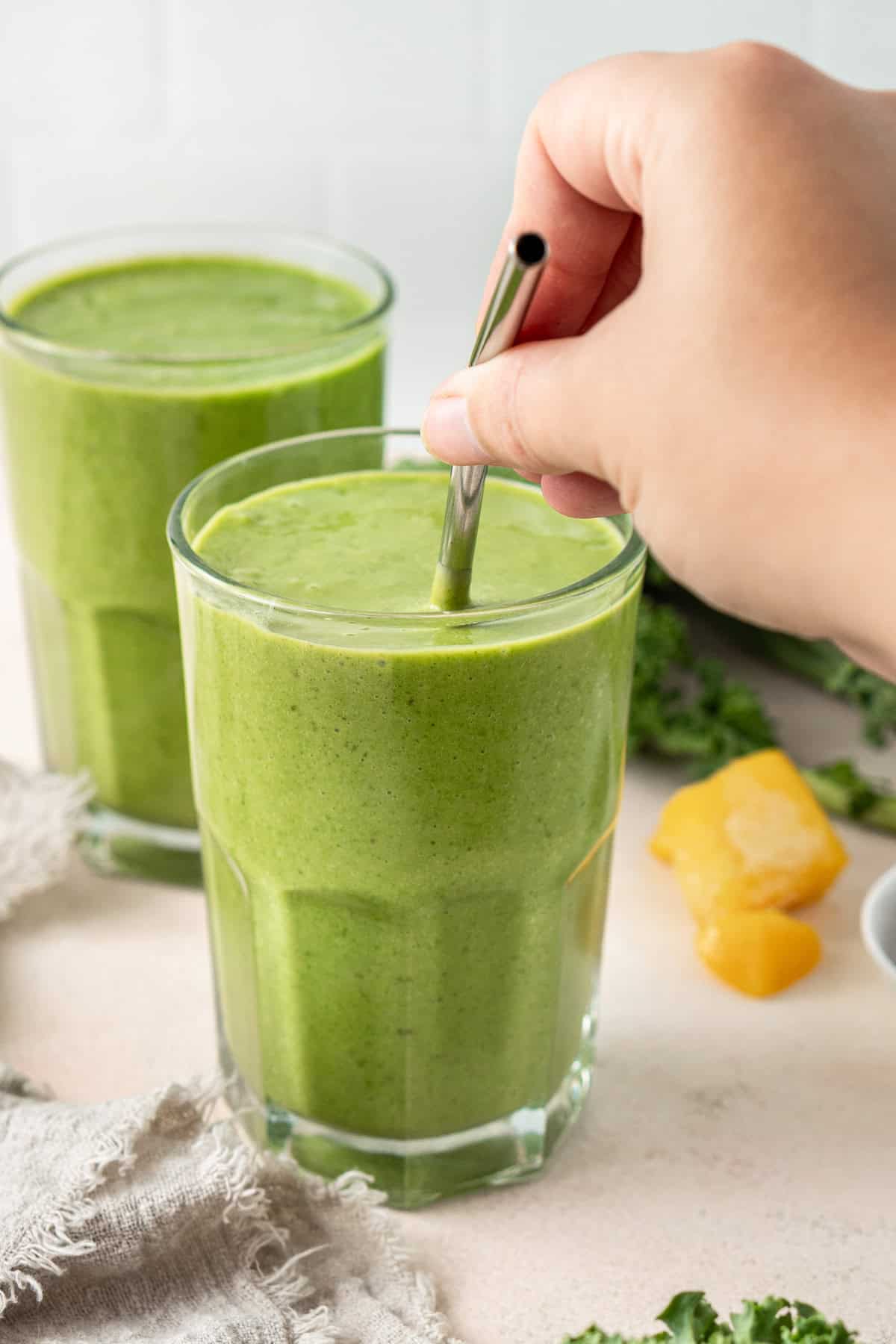 A hand putting a metal straw into a green smoothie.