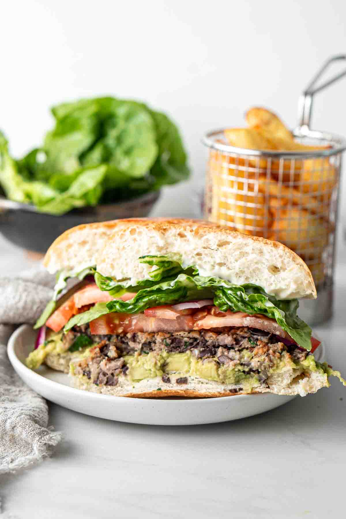 Close up of a black bean burger cut in half showing the layers with chips and salad in the background. 