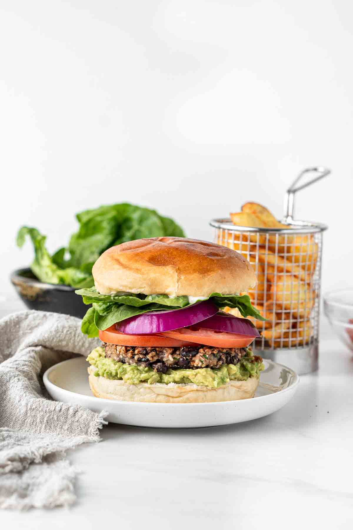 Vegan black bean burger on a plate with chips and salad in the background.