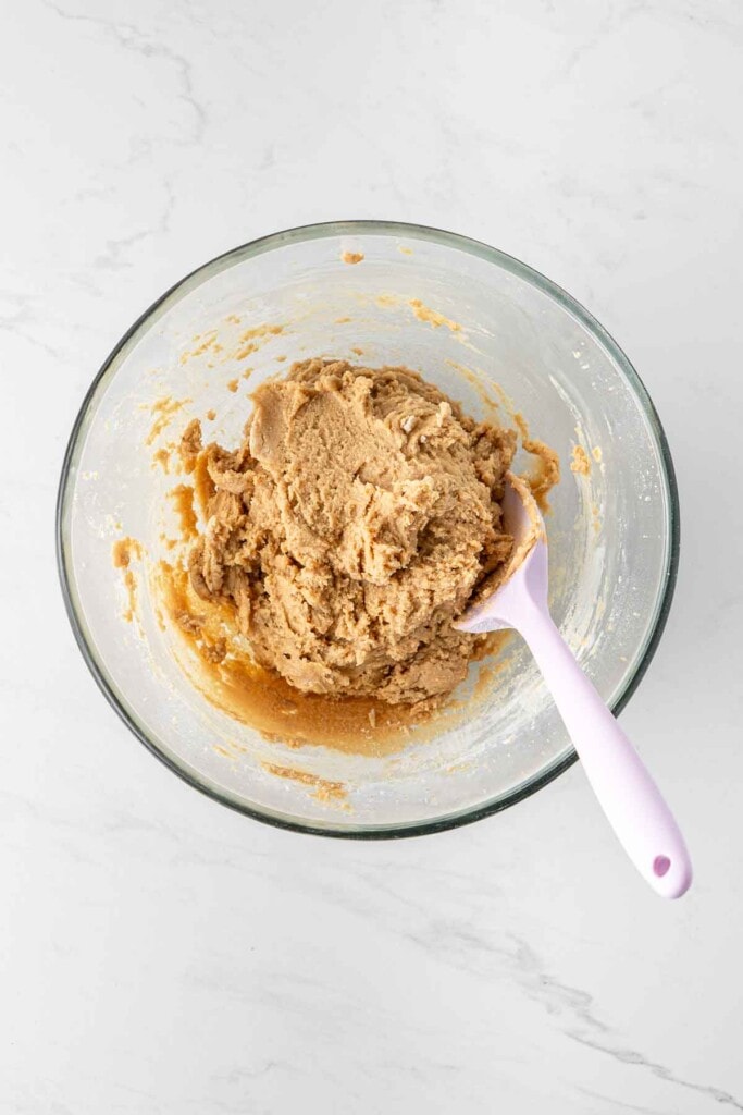 Peanut butter cookie dough in a glass bowl with a spatula. 