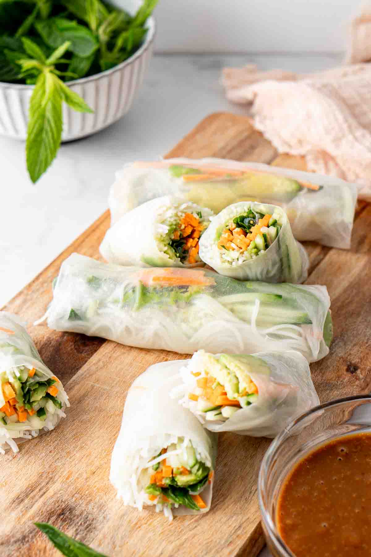 Fresh spring rolls laid out on a wooden serving board with peanut sauce.