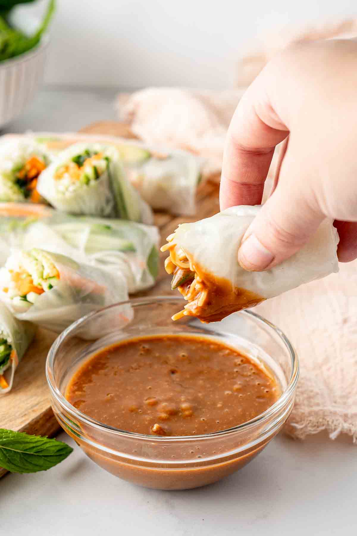 Rice paper roll being dunked in creamy peanut sauce.