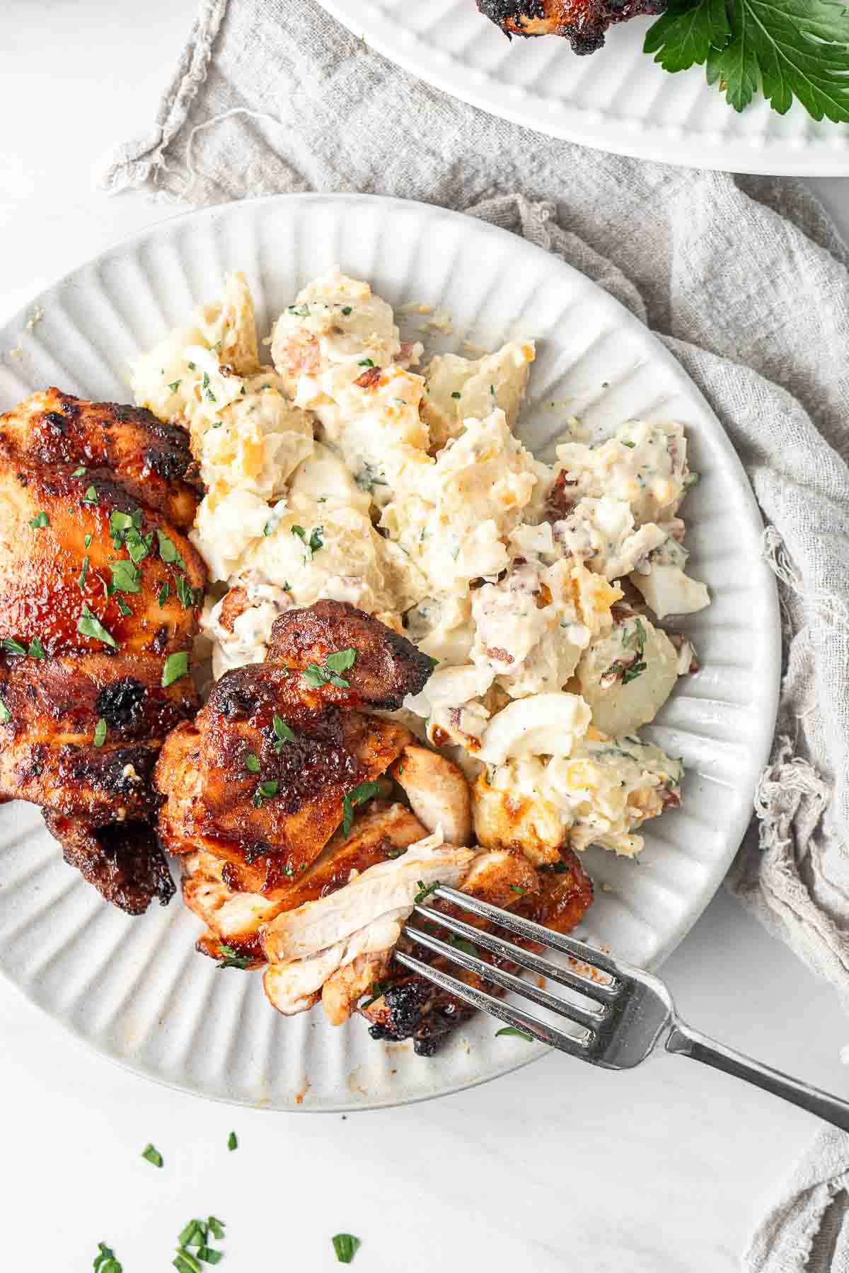 BBQ chicken thighs served on a plate with potato salad. 