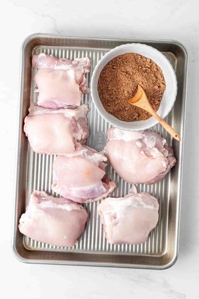 Raw chicken thighs on a tray with the homemade dry rub.