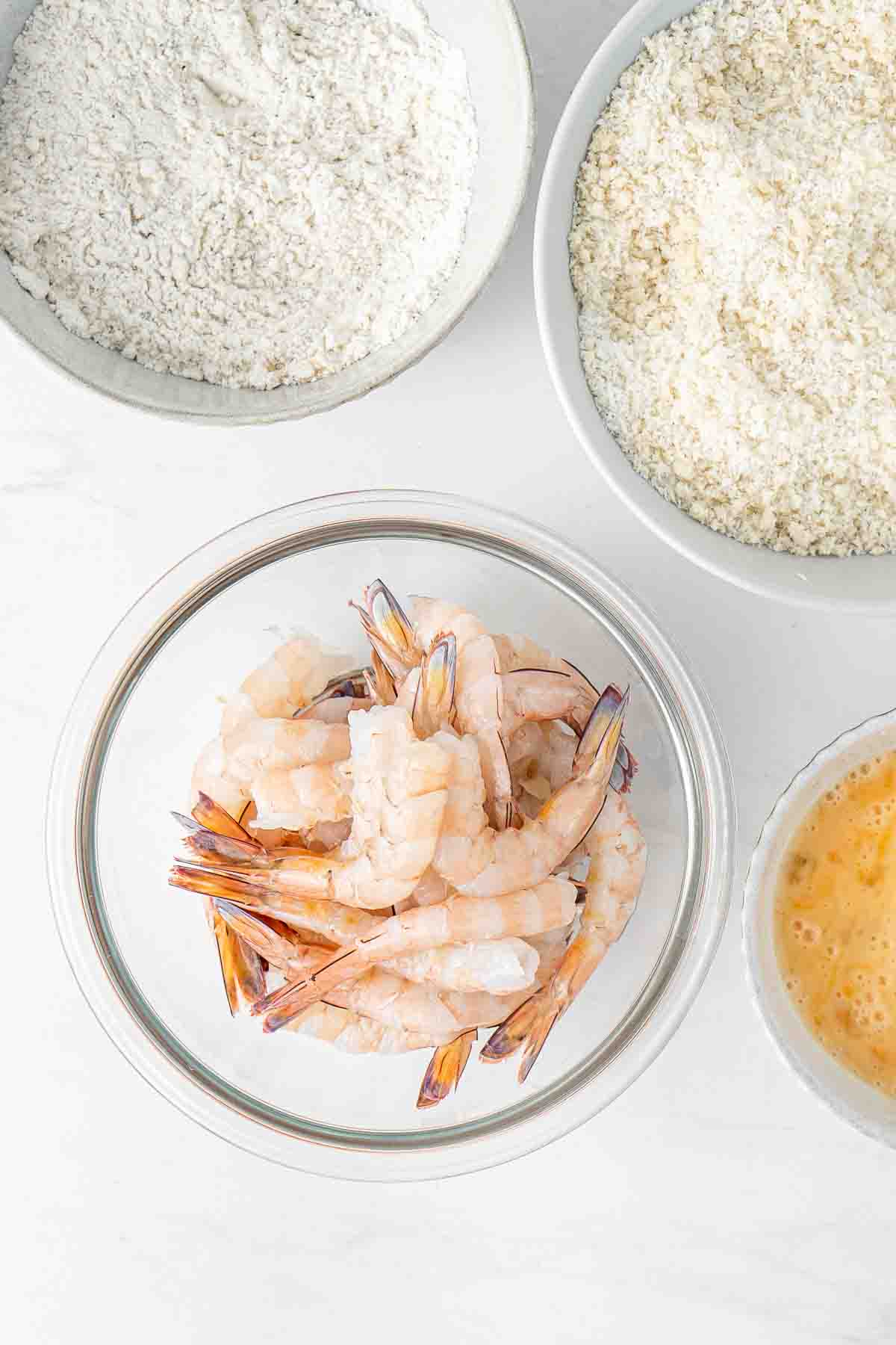 Peeled prawns in a glass bowl with other bowls in the background ready for crumbing.