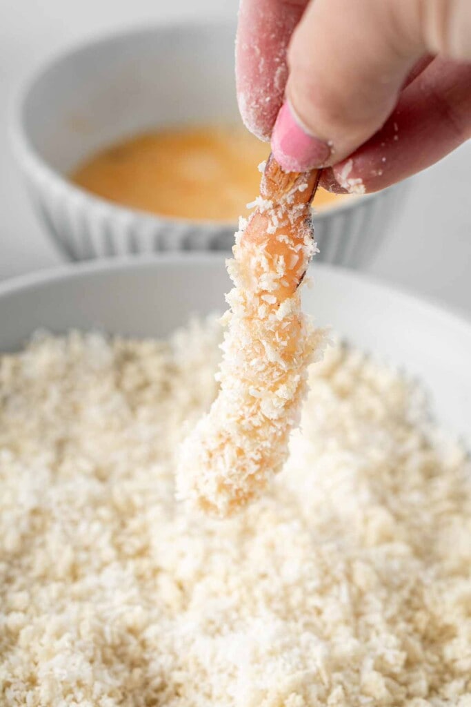Prawn being dipped in panko and coconut mixture.