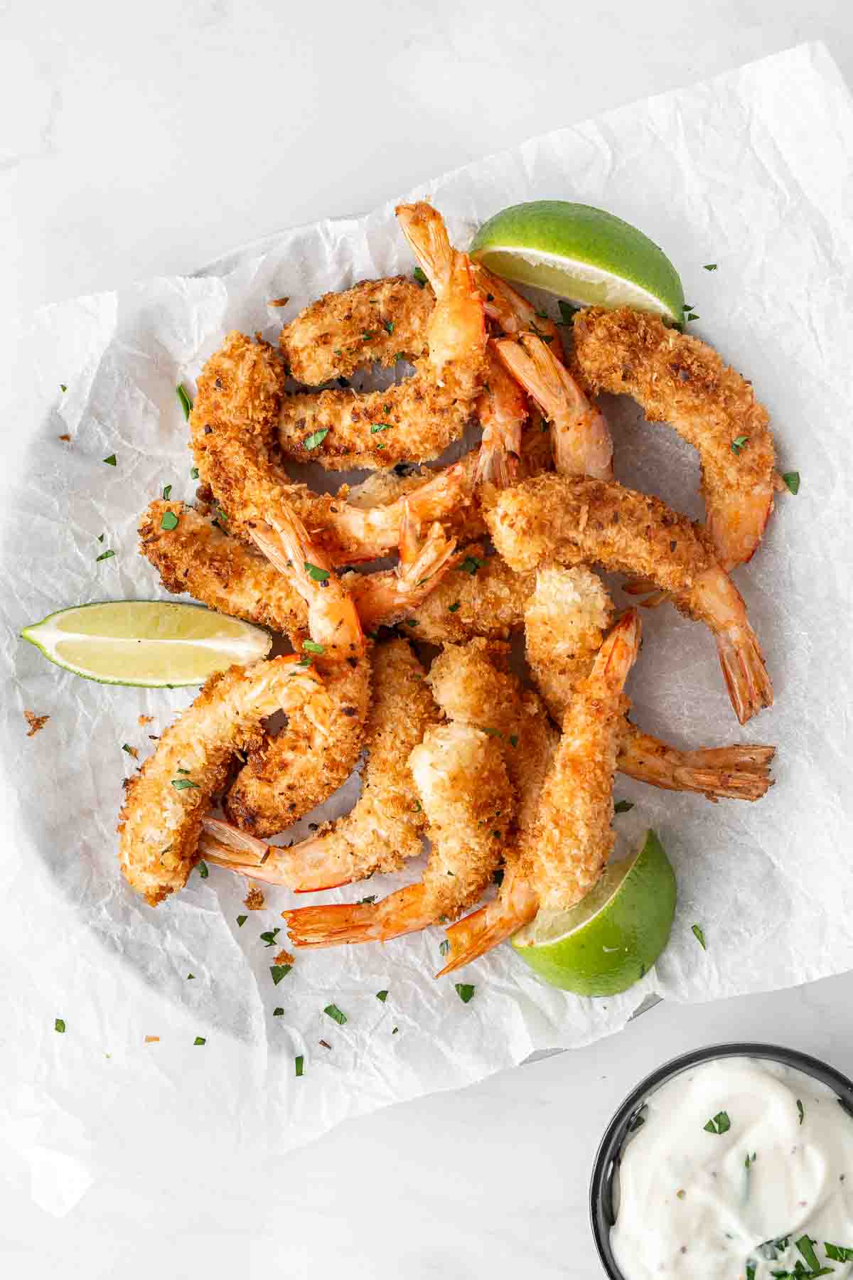 Golden brown coconut prawns on a plate with baking paper and lime slices.