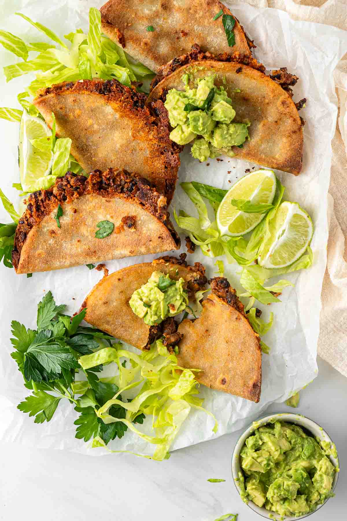 Crispy tacos on a plate from above with avocado and lettuce.