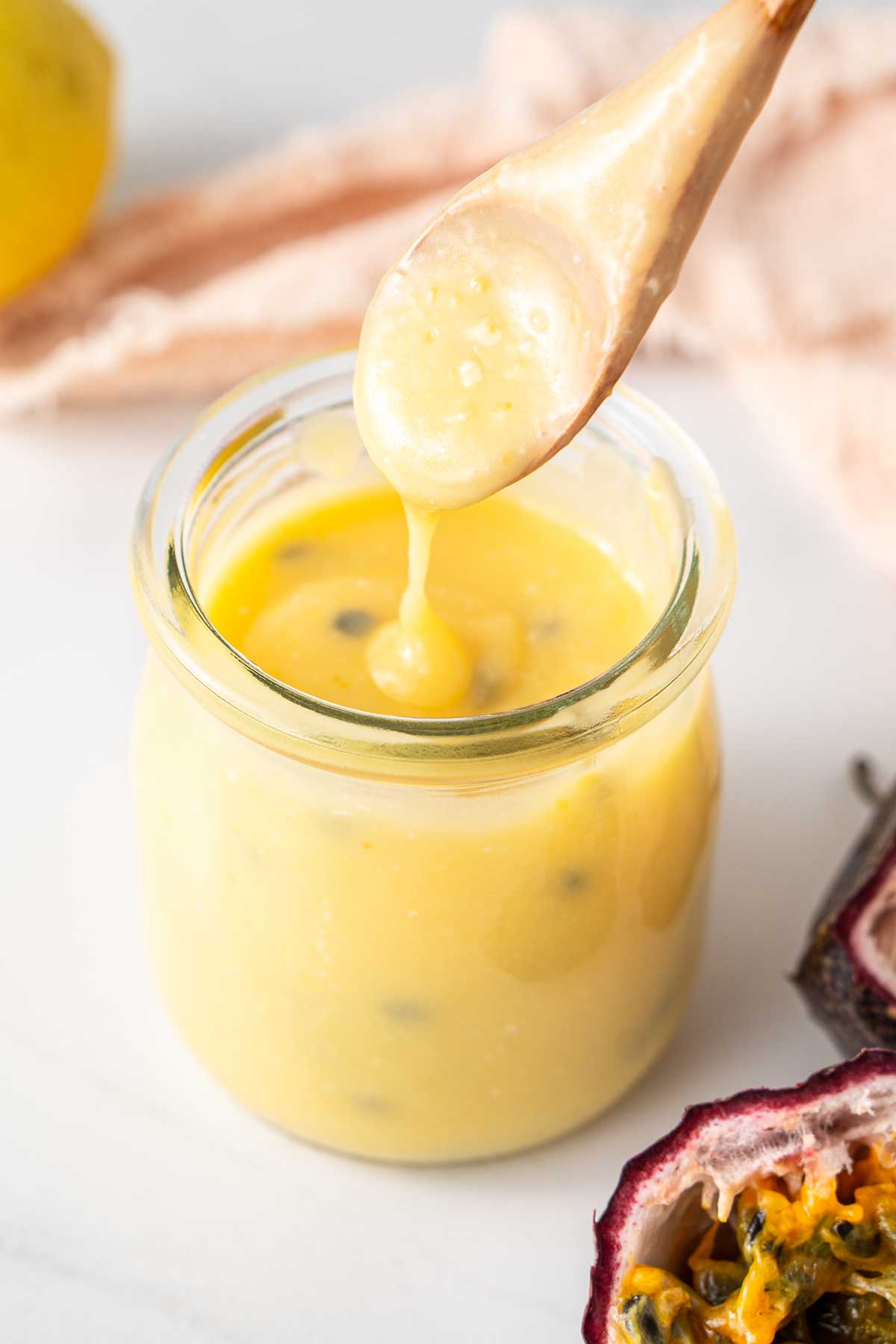 Passionfruit and lemon curd in a jar being drizzled with a spoon.