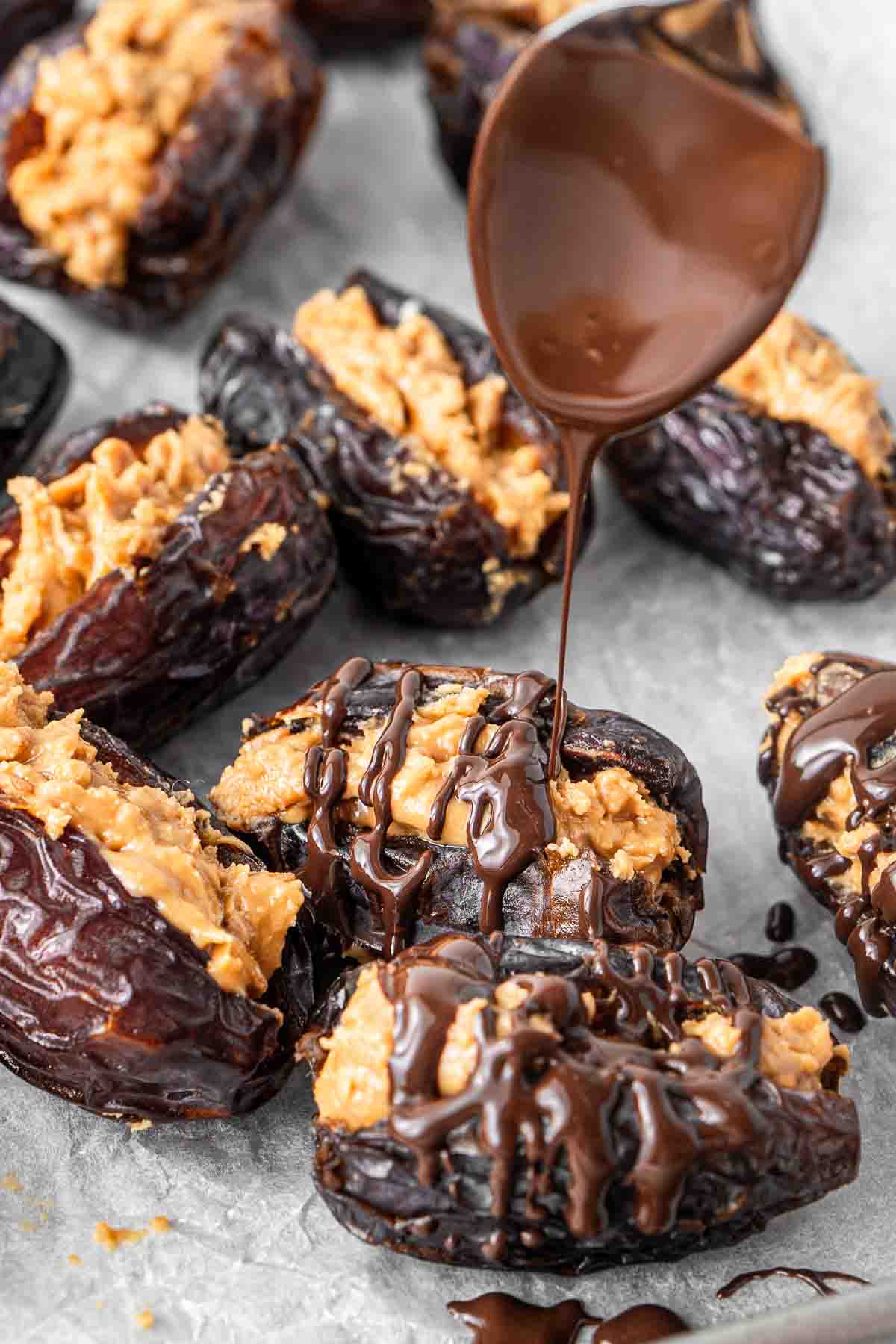 A spoon drizzling melted dark chocolate over the stuffed dates.