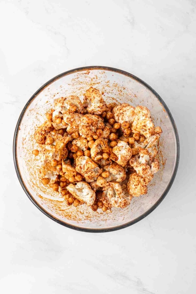 Cauliflower and chickpeas in a large mixing bowl coated in oil and spices.