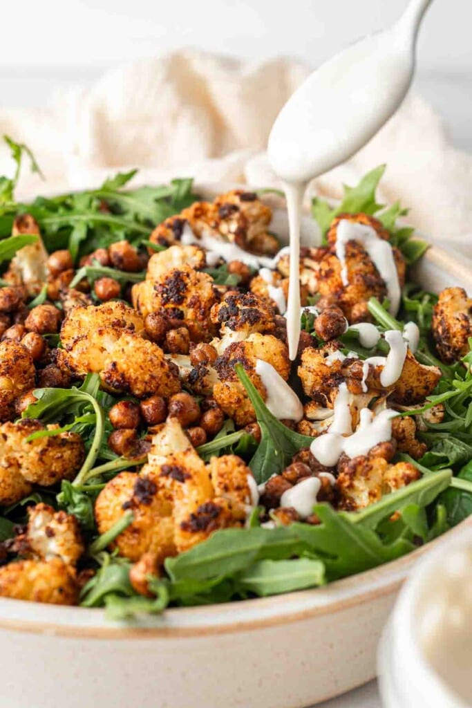 Roasted cauliflower and chickpeas in a bowl with salad greens and garlic tahini dressing.