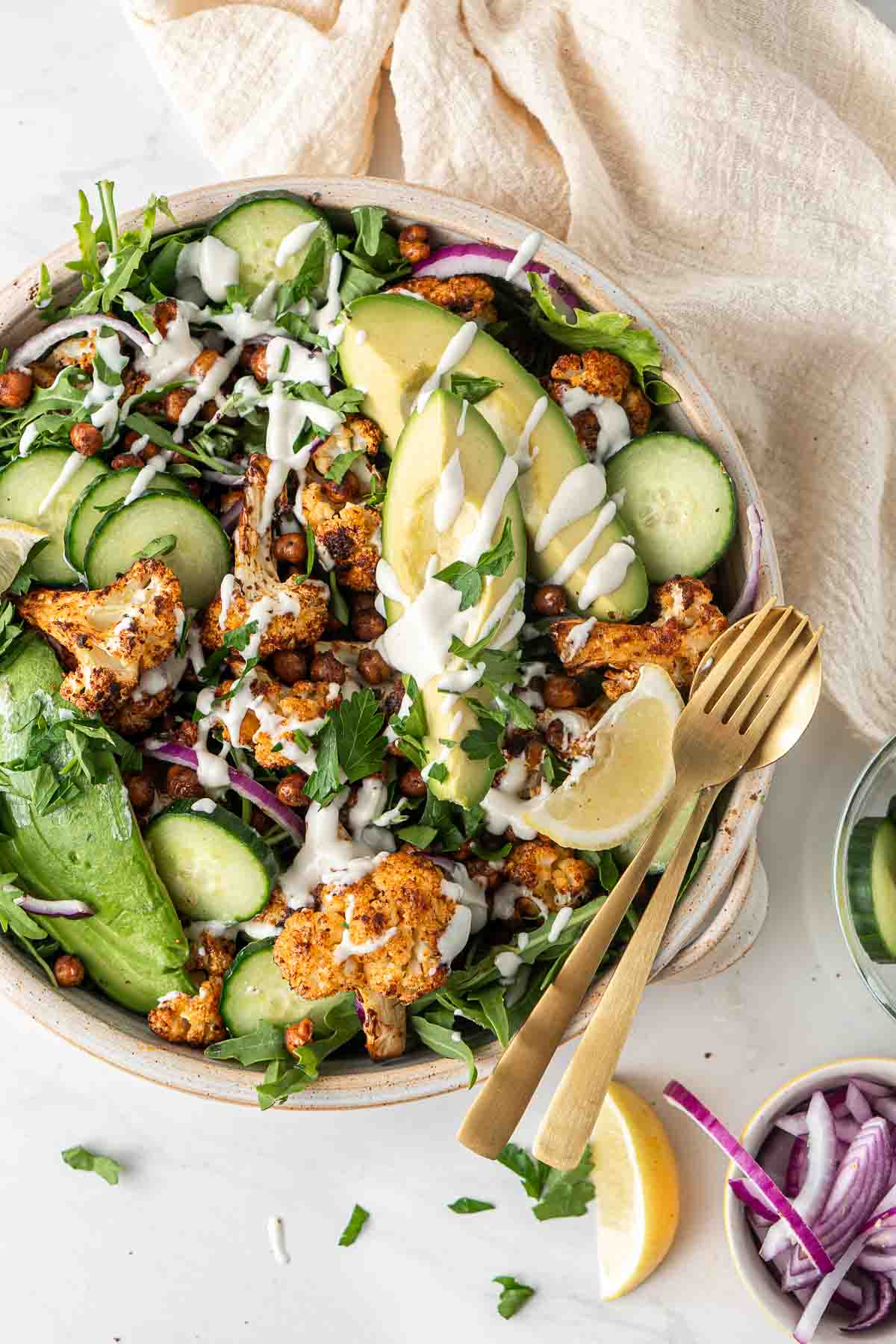 Roasted cauliflower salad in a bowl with avocado and garlic tahini dressing with a gold fork.