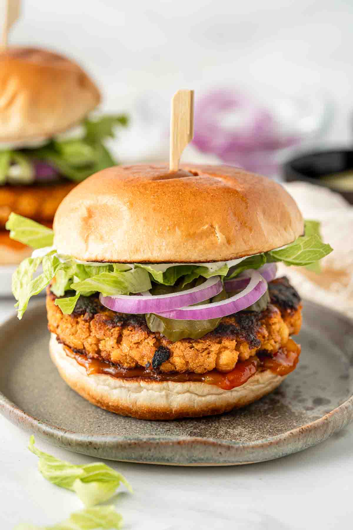 Sweet potato and chickpea burgers on a plate with lettuce, red onion, pickles and tomato relish. 