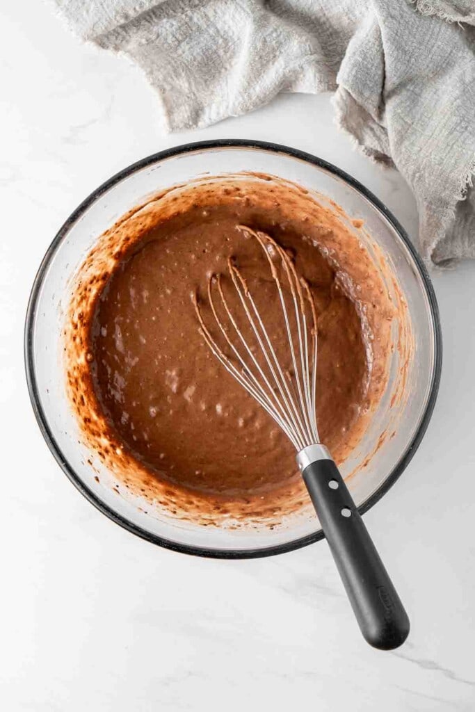 Chocolate pancake batter in a large glass mixing bowl with a whisk.