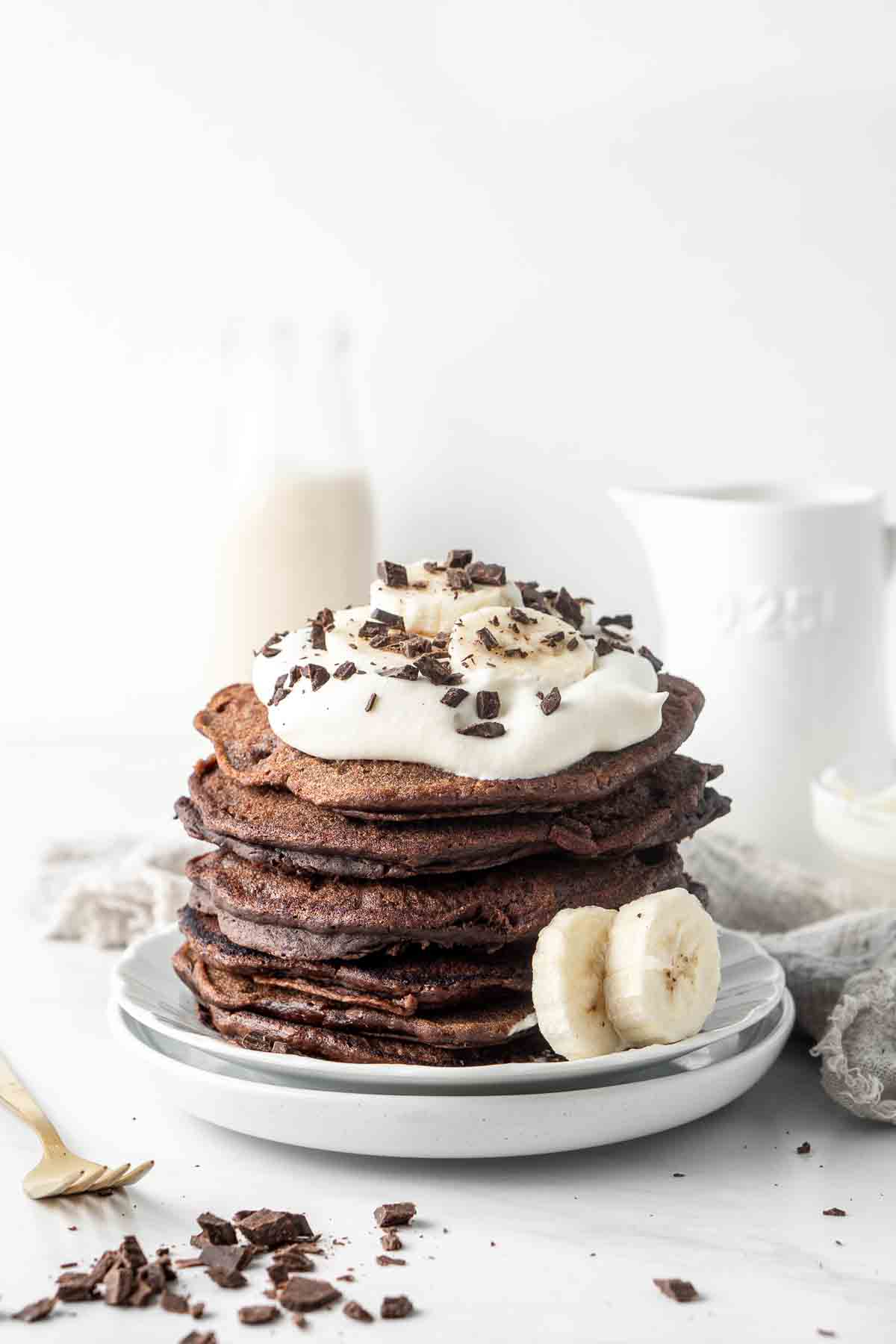 Stack of chocolate pancakes with whipped cream and bananas. 