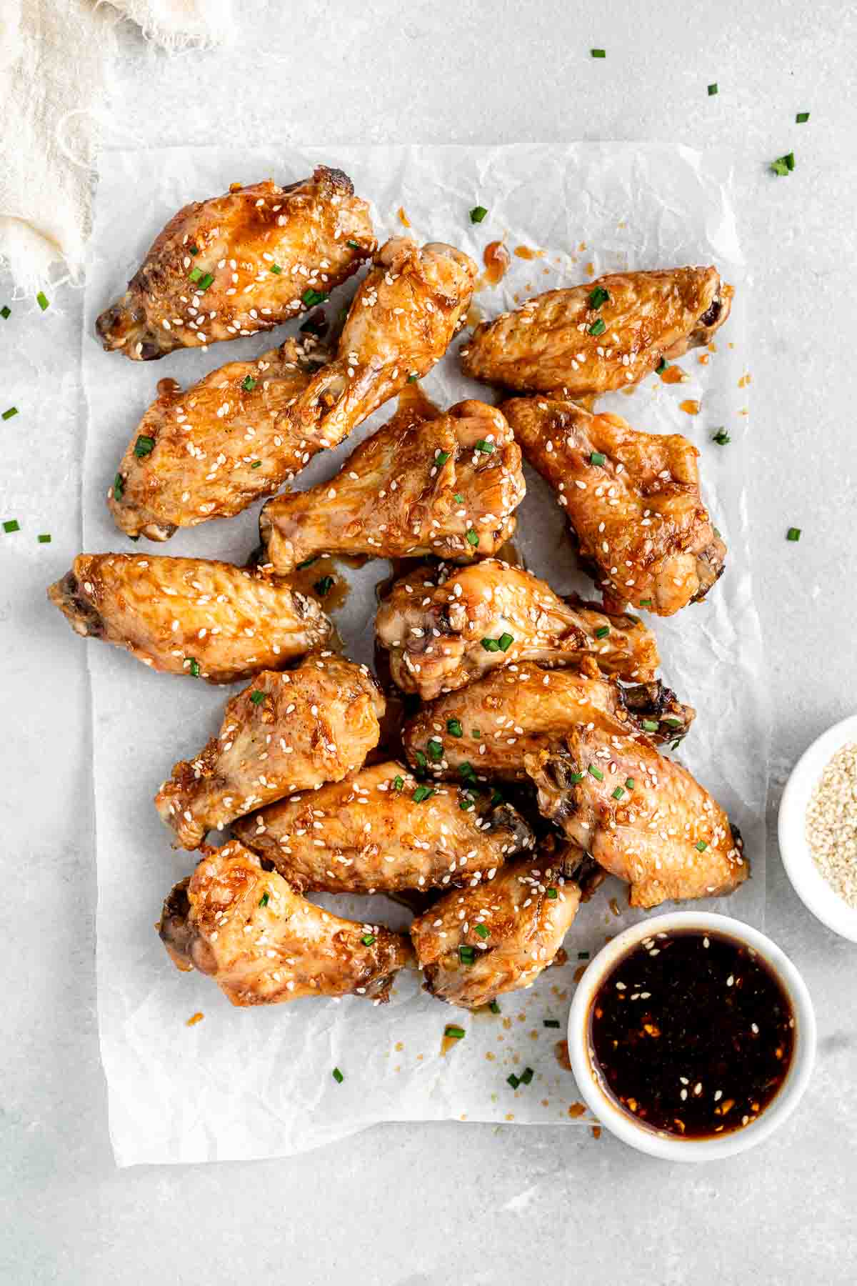 Honey garlic chicken wings with sesame seeds and chives on baking paper.