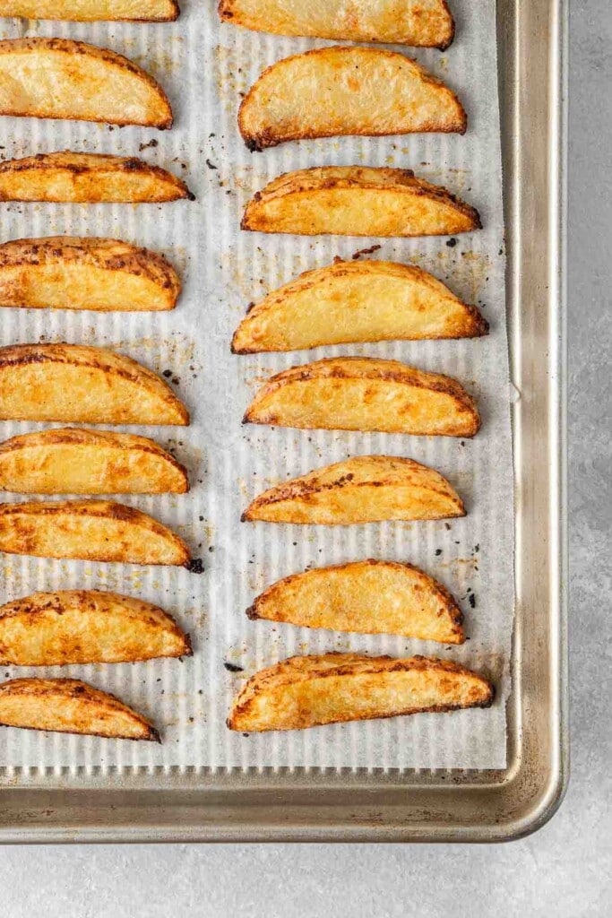 Cooked potato wedges on a baking tray.
